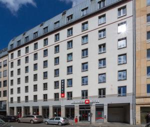 un gran edificio blanco con coches estacionados frente a él en MEININGER Hotel Leipzig Hauptbahnhof en Leipzig