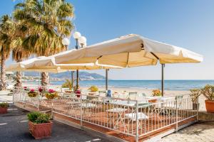 a beach with tables and umbrellas and the ocean at Hotel Tina in Diano Marina