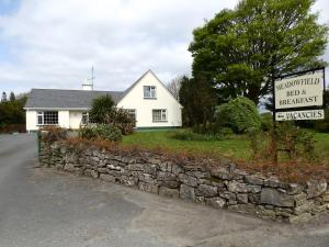 a white house with a stone wall and a sign at Meadowfield in Ballyvaughan