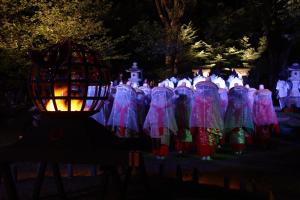 un groupe de personnes vêtues de robes dans un cimetière la nuit dans l'établissement Ashita no Mori, à Hongu