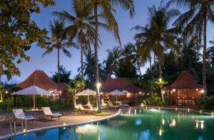 ein Resortpool mit Stühlen und Palmen in der Nacht in der Unterkunft Diamond Beach Villa Lombok in Tanjung