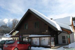 ein schneebedecktes Gebäude mit einem vor der Unterkunft geparkt roten Auto in der Unterkunft Familienappartement Ötscherbär in Lackenhof