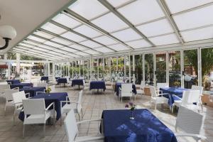 un restaurante con mesas azules, sillas y ventanas blancas en Hotel Ideal Bianchini, en Riccione