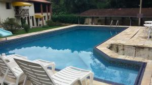 a swimming pool with white chairs and a table at Abaete Pousada da Estancia in São Roque