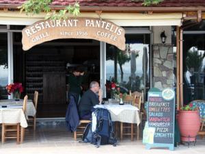 Ein Mann, der vor einem Restaurant an einem Tisch sitzt. in der Unterkunft Pantelis in Póros