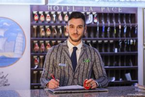 un homme debout à un comptoir tenant un stylo dans l'établissement Hotel La Pace, à Pise