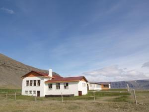 a white house in a field with mountains in the background at Hotel Latrabjarg in Örlygshöfn