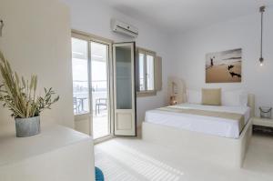 a white bedroom with a bed and a balcony at Muses in Aegiali