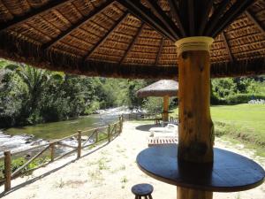 a table with a straw umbrella next to a river at Pousada Chácara do Rio in Lumiar