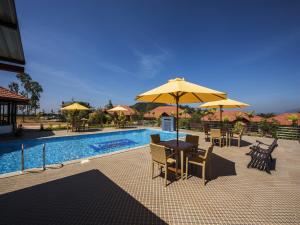 um pátio com uma mesa e guarda-sol ao lado de uma piscina em Woodstock Resorts em Madikeri