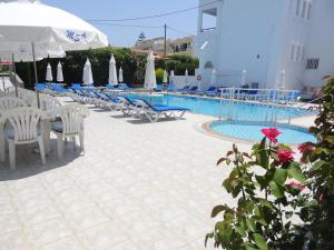 a pool with chairs and umbrellas and a table with a flower at Michalis Studios & Apartments in Kos
