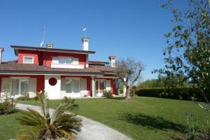 une maison rouge et blanche avec une cour verdoyante dans l'établissement DIMORA Simona, à Caorle