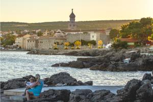 a woman and child sitting on rocks near the water at Hotel Bor in Krk