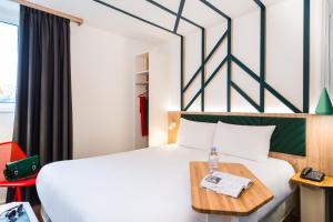 Cette chambre comprend un lit blanc et une table. dans l'établissement ibis Styles Rouen Val De Reuil, à Val de Reuil