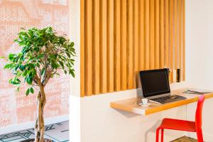 - un bureau avec un ordinateur portable, une chaise et un arbre dans l'établissement ibis Styles Rouen Val De Reuil, à Val de Reuil