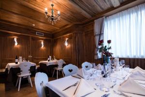 un comedor con mesas y sillas blancas y una lámpara de araña en Hotel Collini, en Pinzolo