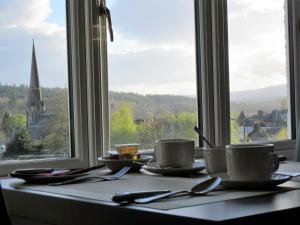 une table avec des tasses et des soucoupes devant une fenêtre dans l'établissement The Knowe Guest House, à Callander