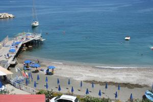 a beach with blue umbrellas and a pier with a boat at Hotel Baia Di Puolo in Massa Lubrense