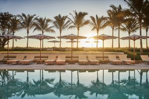 einen Pool mit Stühlen, Sonnenschirmen und Palmen in der Unterkunft Four Seasons Hotel at The Surf Club in Miami Beach