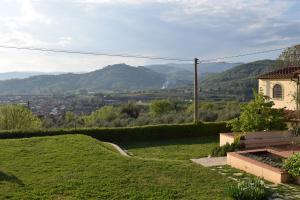 a green hill with a house and mountains in the background at La Valle dei Gobbi in Monsummano Terme