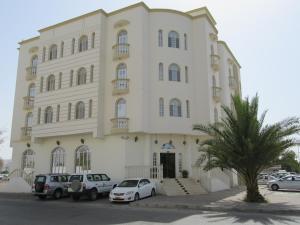 un grande edificio bianco con auto parcheggiate di fronte di Al Ferdous Hotel Apartments a Mascate