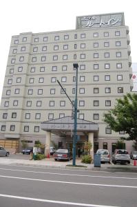 un gran edificio blanco con coches estacionados frente a él en Hotel Route-Inn Obihiro Ekimae en Obihiro