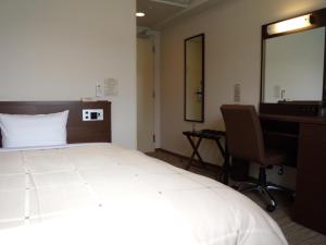 a hotel room with a bed and a desk and a mirror at Hotel Route-Inn Tsuruoka Ekimae in Tsuruoka