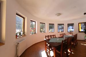uma sala de jantar com mesa, cadeiras e janelas em Vila Gal em Lacul Roșu