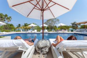 a group of people laying on beds next to a pool at Naïa Resort and Spa in Placencia Village