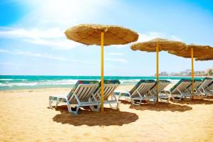 a group of chairs and umbrellas on a beach at Anna & Pierre-Noel apartment. in Benalmádena