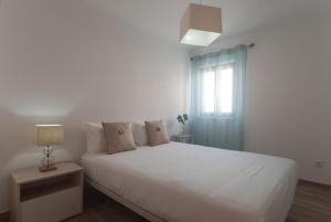 a white bedroom with a white bed and a window at WestSide Beach House in Peniche de Cima
