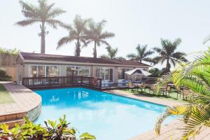 Umtentweni的住宿－樹下酒店及會議中心，棕榈树屋前的游泳池