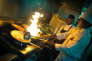 two chefs in a kitchen preparing food on fire at Heritage Park Hotel in Honiara