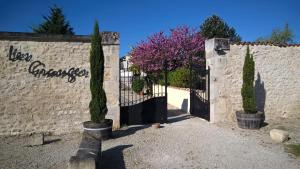 une porte dans un mur en pierre avec des arbres et des fleurs violettes dans l'établissement Domaine Les Granges, à Saint-Jean-dʼAngély