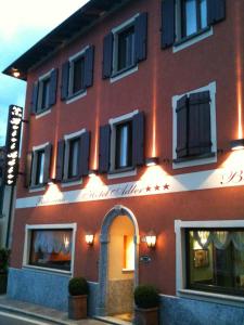 a red building with black shuttered windows on a street at Hotel Adler in Menaggio