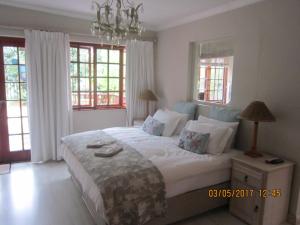 a bedroom with a large white bed with windows at Twilight Cottage in Plettenberg Bay