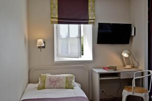Habitación pequeña con cama, escritorio y ventana. en Hôtel Les Bains de Secours, en Sévignacq-Meyracq