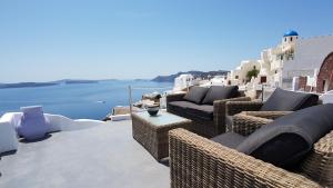 eine Terrasse mit Korbstühlen, Tischen und Wasser in der Unterkunft Aqua & Terra Traditional Cave Houses in Oia