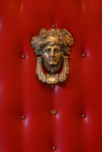 un bouton de porte dorée avec un visage sur une porte rouge dans l'établissement Hôtel Marie-Rollet, à Québec