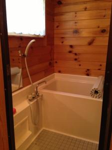 ein Badezimmer mit einer Badewanne und einer Holzwand in der Unterkunft Hakuba Cottage Gram in Hakuba