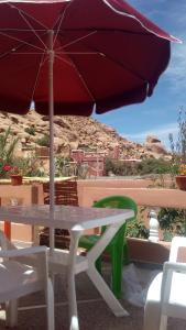 un tavolo bianco con ombrellone e sedie rossi di Maison d'accueil Wakrim a Tafraout