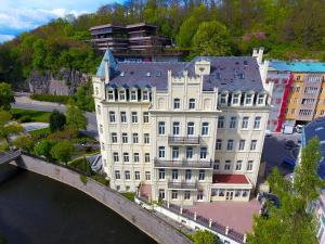 a large white building next to a river with a bridge at Hotel Pavlov in Karlovy Vary
