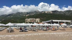 una playa con sillas, sombrillas blancas y una montaña en ApartHotel Belvedere Residence Becici Budva, en Budva