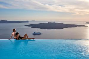 a woman sitting on the edge of a swimming pool looking out at the ocean at Cosmopolitan Suites - Small Luxury Hotels of the World in Fira