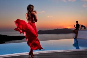 une femme en robe rouge marchant près d'une piscine dans l'établissement Cosmopolitan Suites - Small Luxury Hotels of the World, à Fira