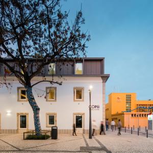 um edifício com uma árvore em frente em Hostel Conii & Suites Algarve em Quarteira