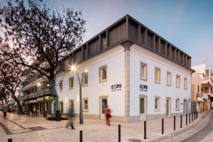 a white building with a black roof on a street at Hostel Conii & Suites Algarve in Quarteira