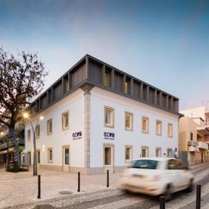 un coche pasando por un edificio blanco en Hostel Conii & Suites Algarve en Quarteira