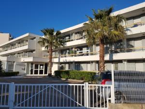 an apartment building with palm trees in a parking lot at Plein cœur du Grau du Roi - Les Cigales de la Mer - 100m de la plage in Le Grau-du-Roi