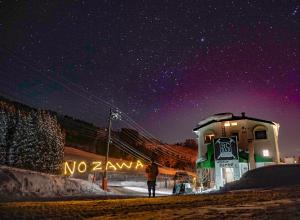 a man standing in front of a nozawa sign at night at The Schneider Hotel in Nozawa Onsen